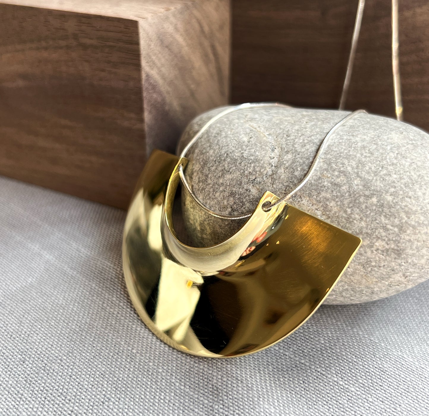 side angle brass pendant laying flat facing left propped up on a grey rock