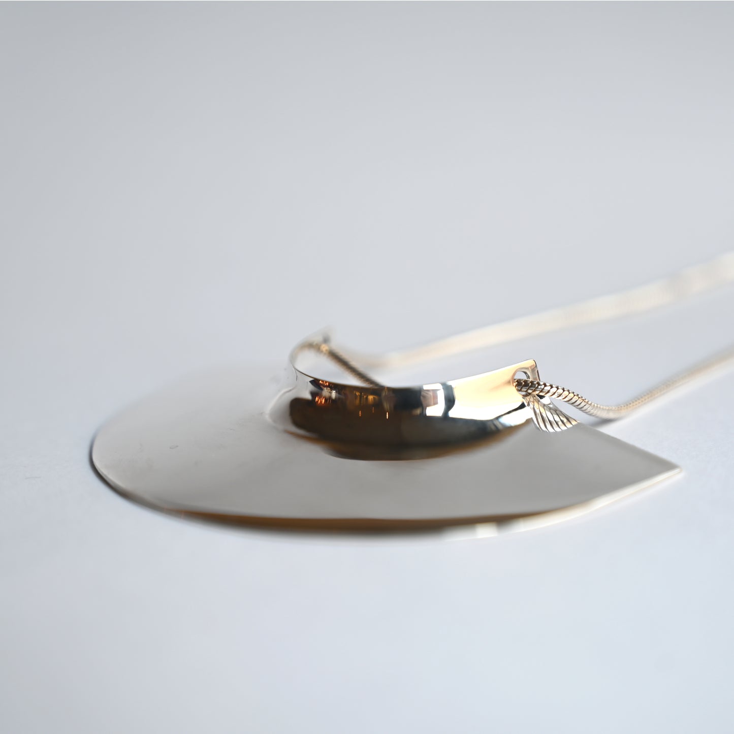 brass pendant laying flat facing slightly left on a white background, close up