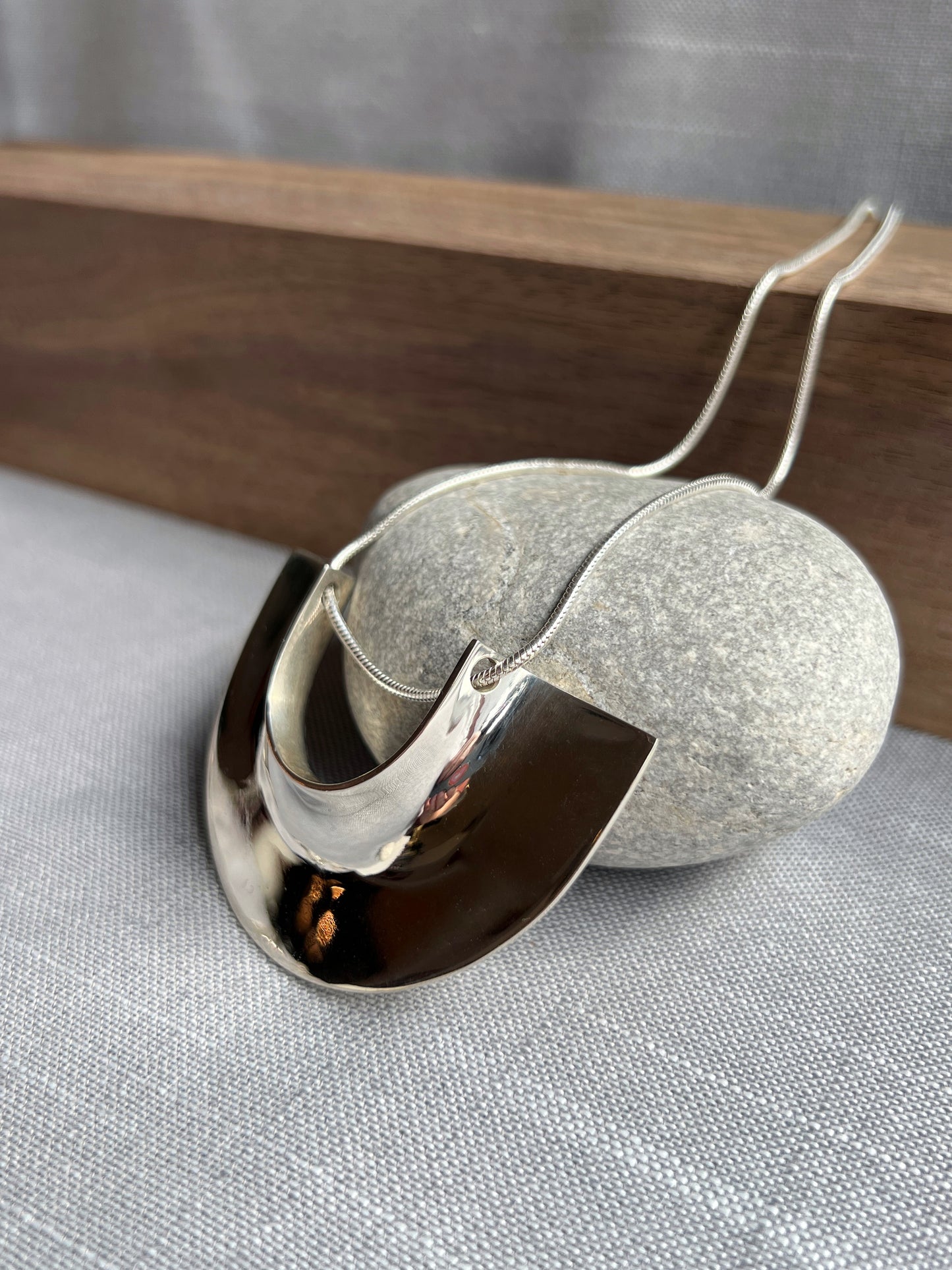 side angle silver pendant laying flat facing left propped up on a grey rock