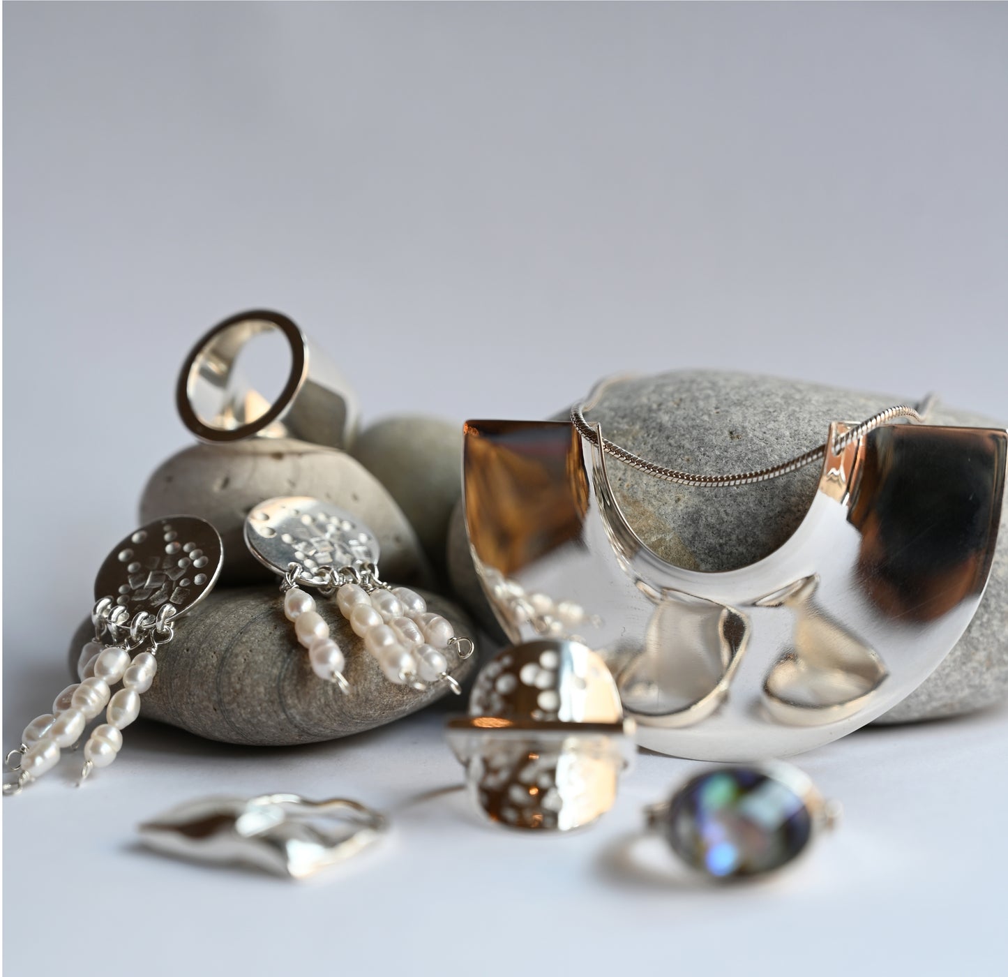 a collection of rings, earrings and necklaces propped up against or ontop of grey rocks. 3 rings are in the foreground and blurred