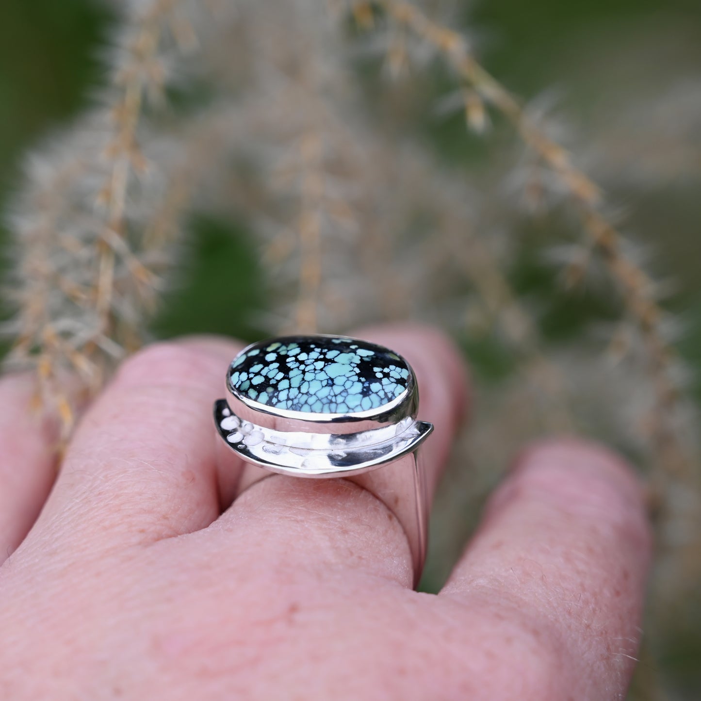 close up of the ring on a middle finger with a blurred green plant background