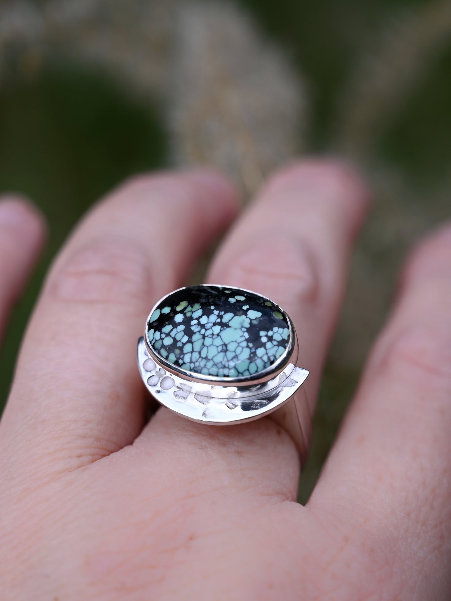 a component hubei turquoise ring on a middle finger with blurred greenery plant background