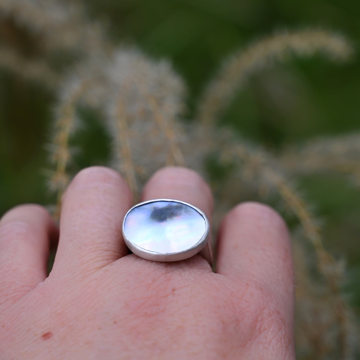 closer up shot of mabe pearl ring on middle finger with greenery and plant background