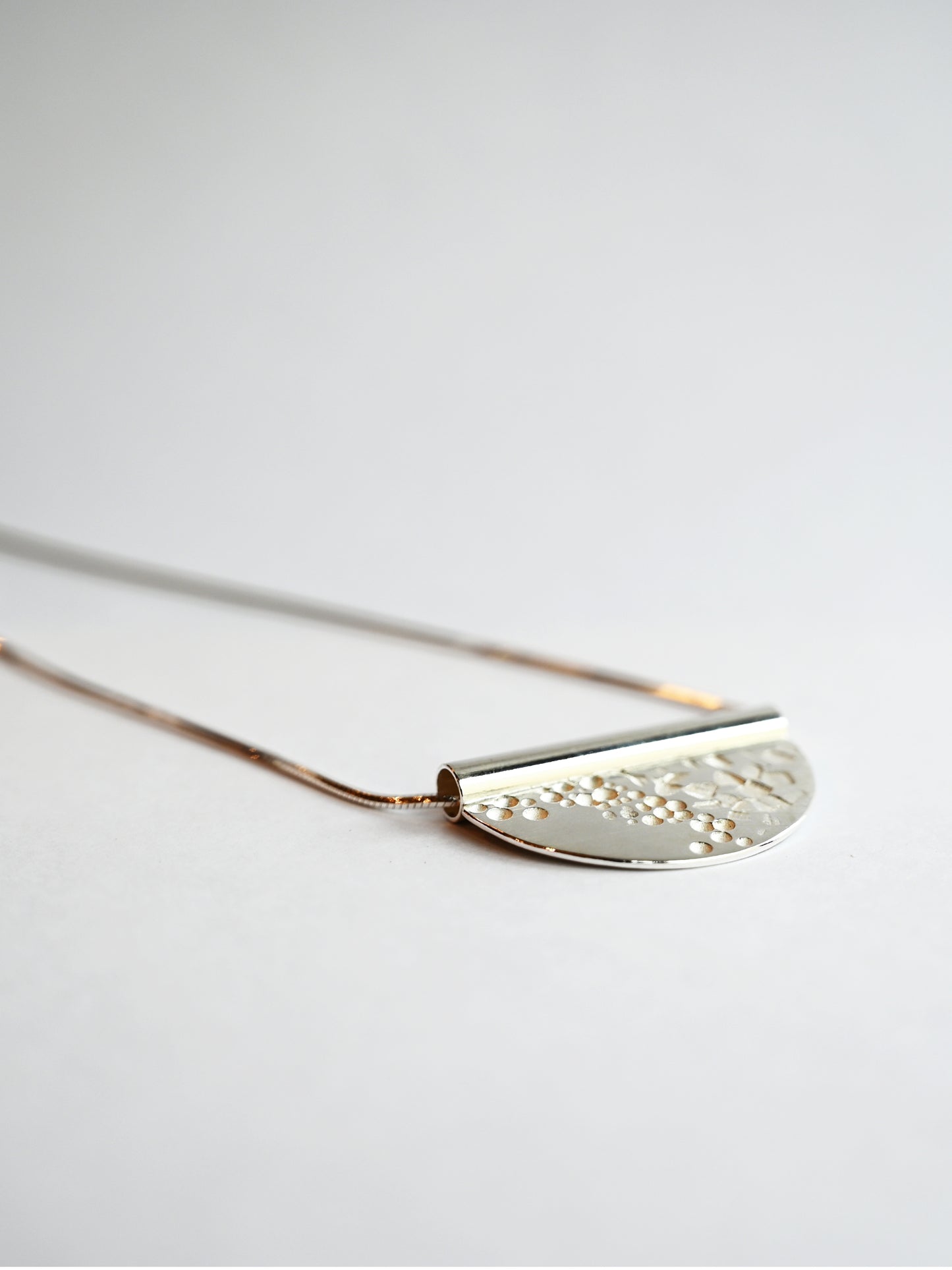 bronze tube necklace laying flat facing to the right on a ground eye level angle with a white background