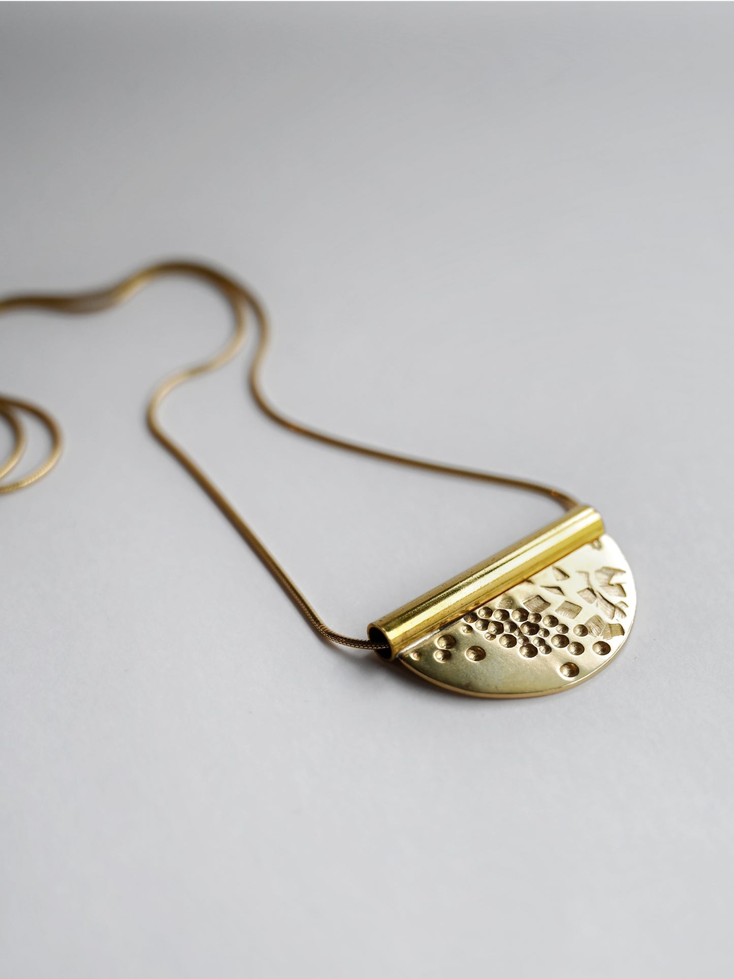 bronze tube necklace laying flat facing to the right on an angle with a white background