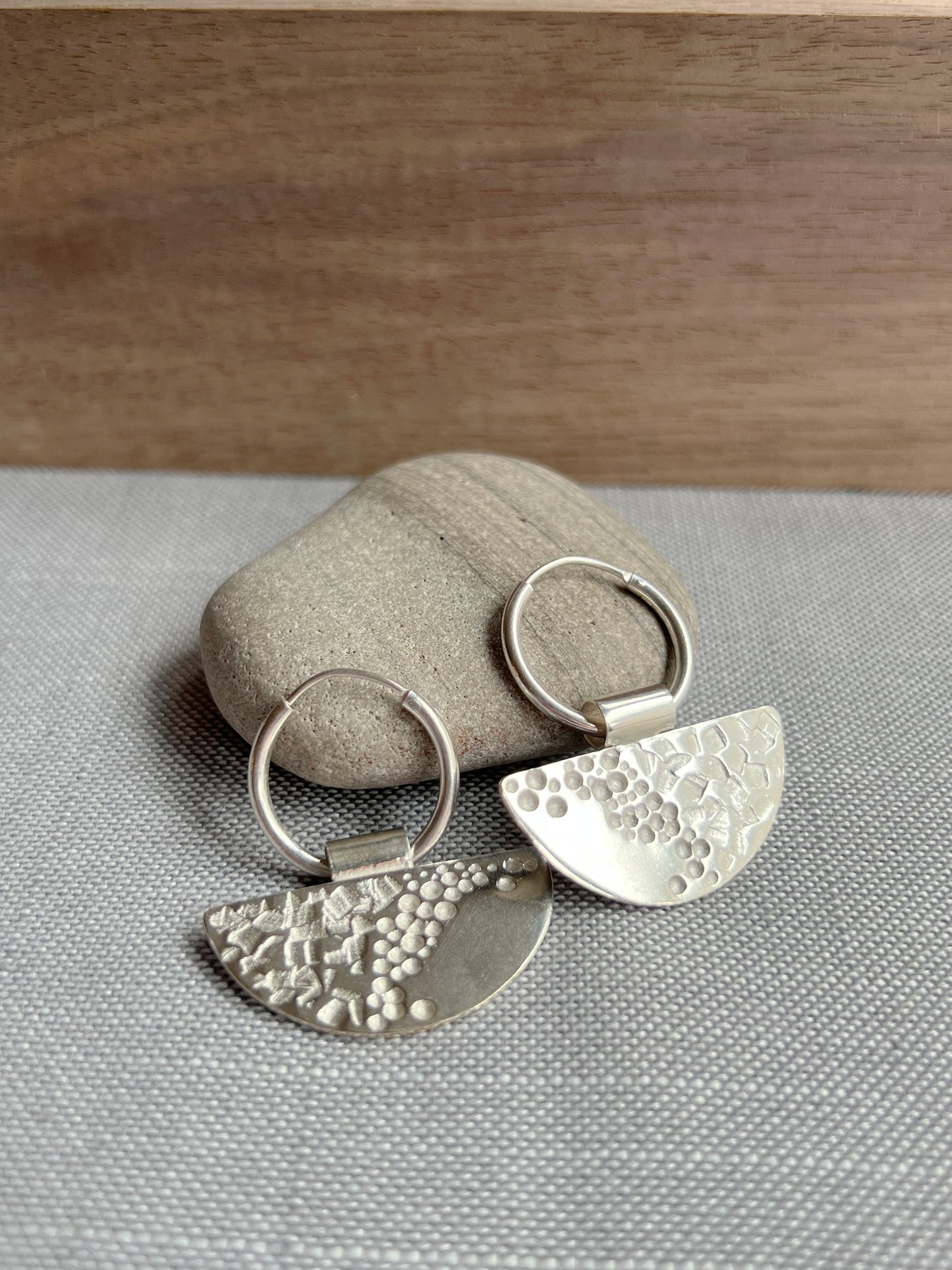 half moon disc hoops laying propped up against a grey rock with a piece of dark wood blurred in the background