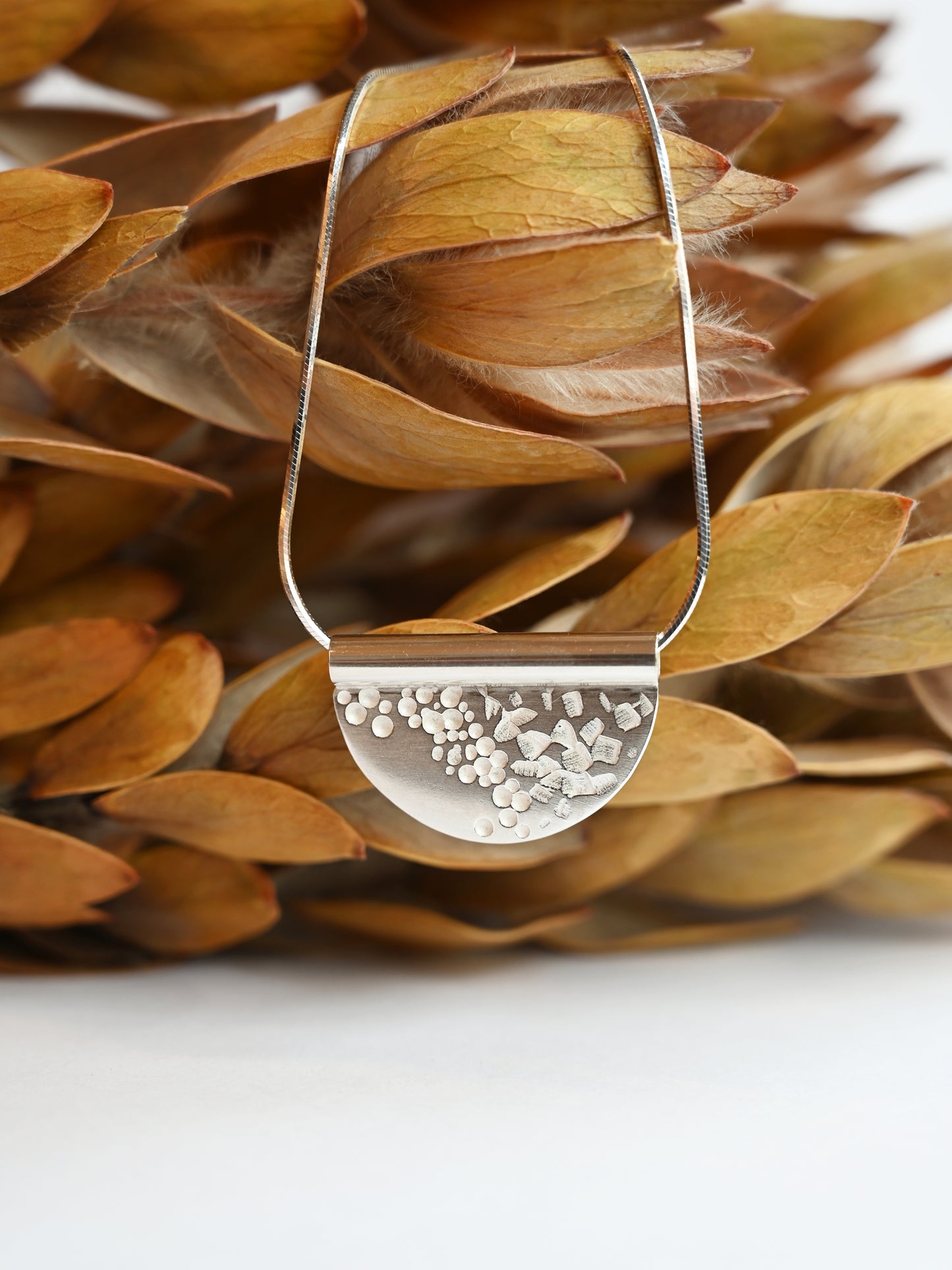sterling silver tube necklace hung up against dry yellow leafs with a white background