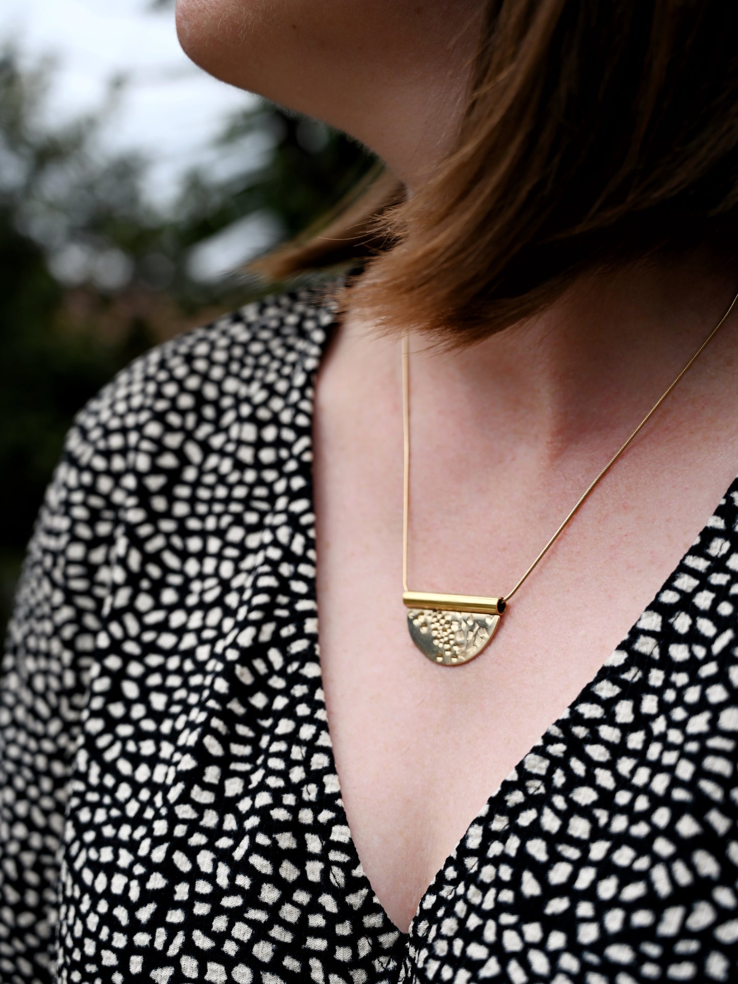 Contrast tube bronze pendant on neck with model looking side ways