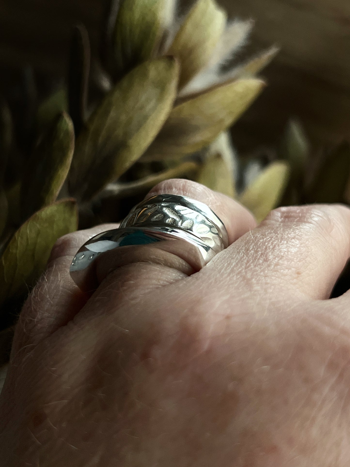 a few stacked silver rings on a ring finger with plants blurred in the background