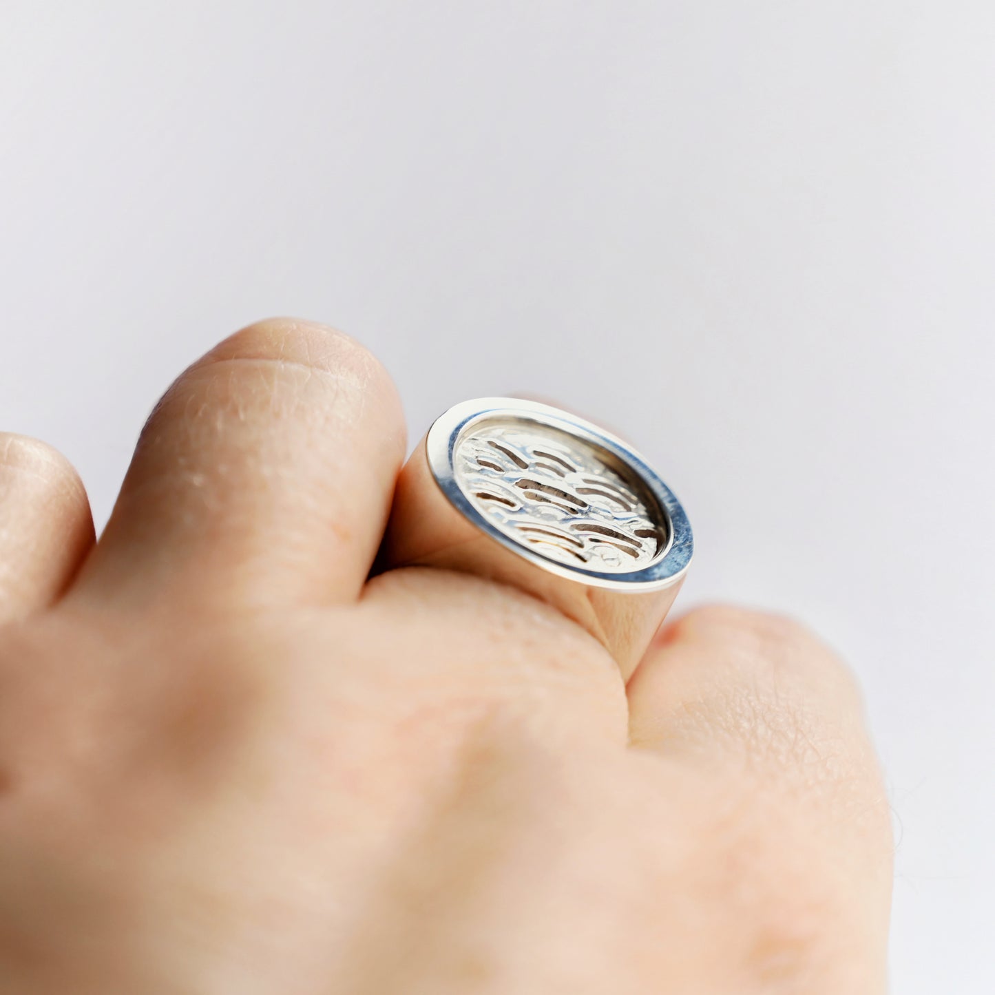 Close-up of a hand wearing a silver node ring with a wave design on a white background