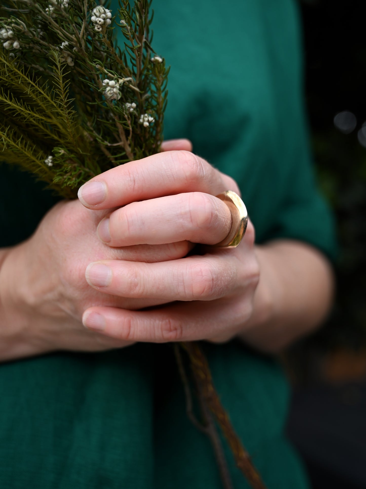Element 1 ring in bronze on middle finger with side view, model holding greenery and wearing green blouse