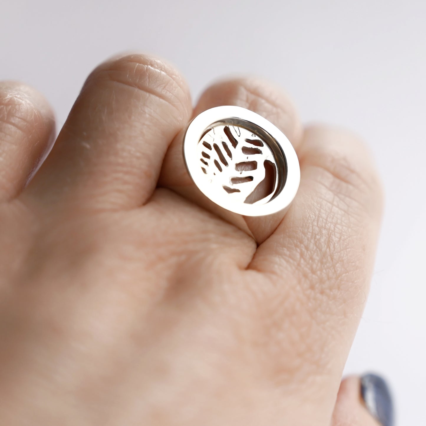 Top view of silver node ring with leaf cut out on hand with white background