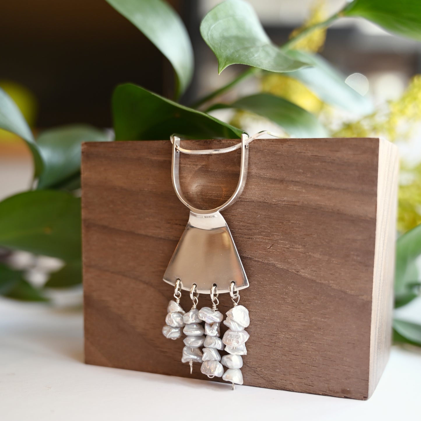 Art deco pendant in silver with pearls hanging on wood block with greenery in background