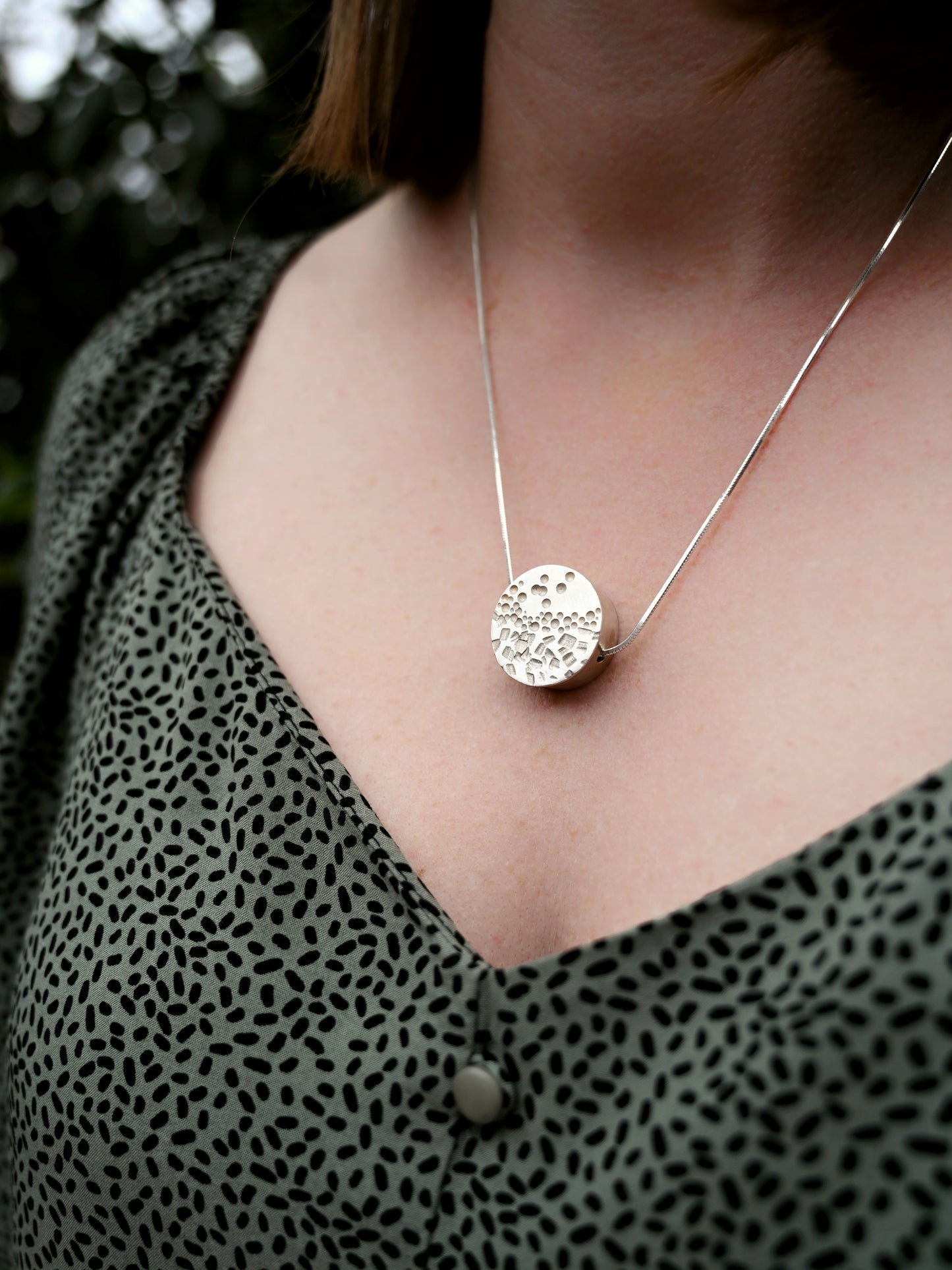 Contrast box pendant in silver around model's neck front view with grey/green blouse with black spots
