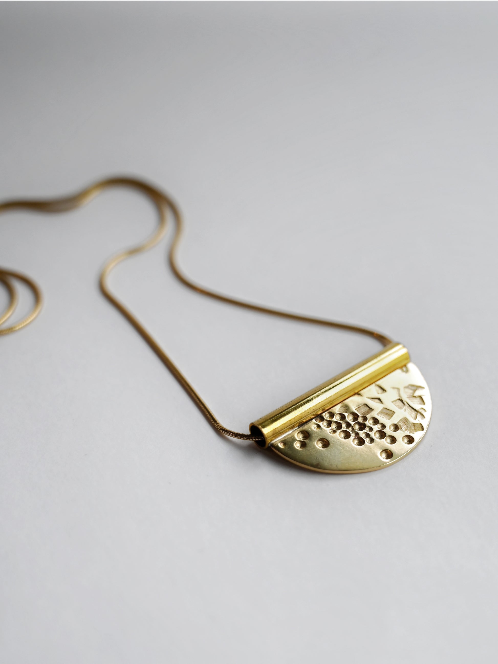 bronze tube necklace laying flat facing to the right on an angle with a white background