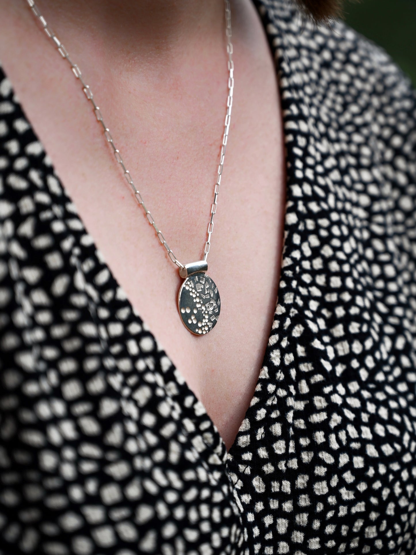 contrast disc pendant in silver around model's neck black and white blouse