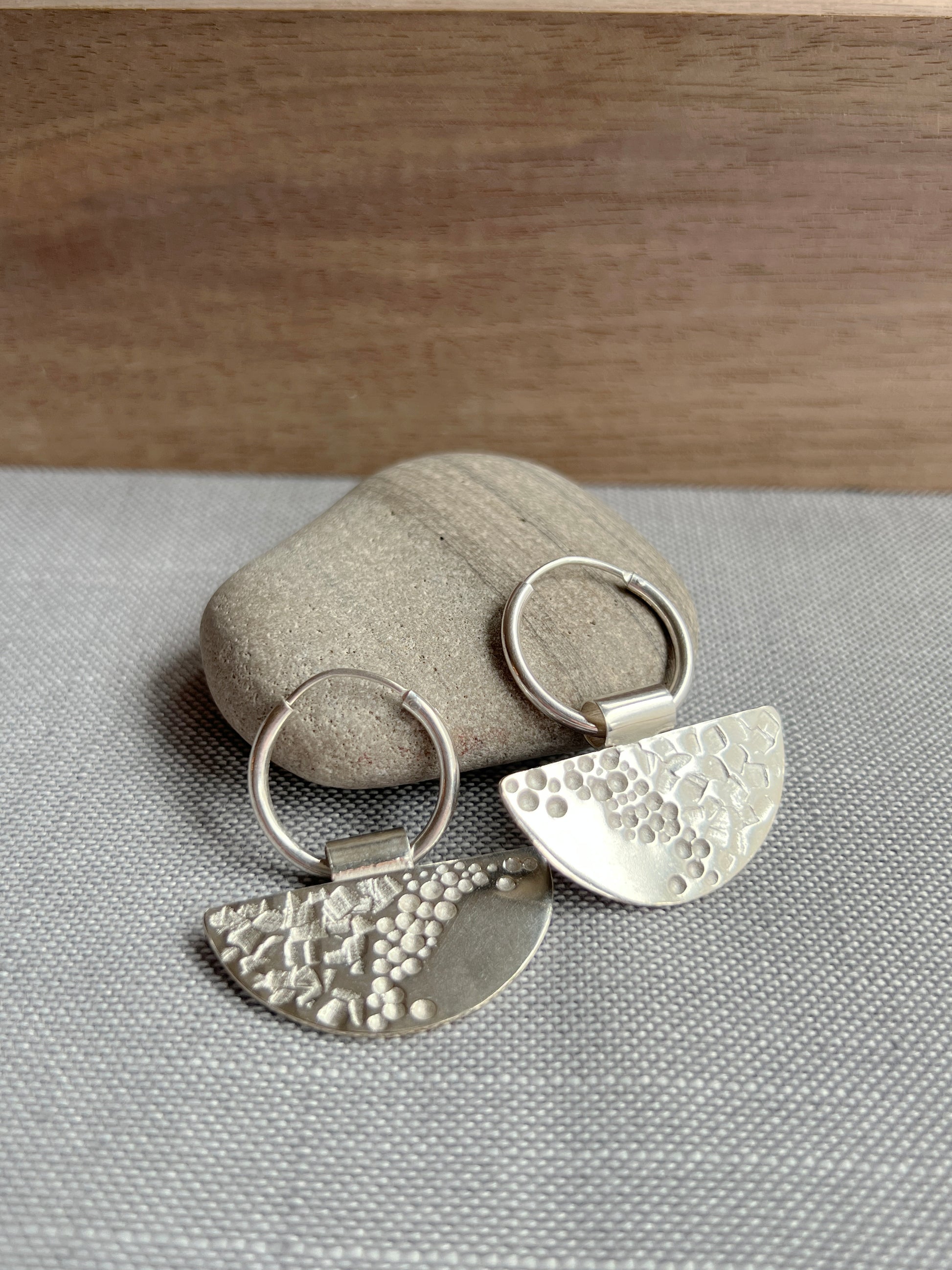 half moon disc hoops laying propped up against a grey rock with a piece of dark wood blurred in the background