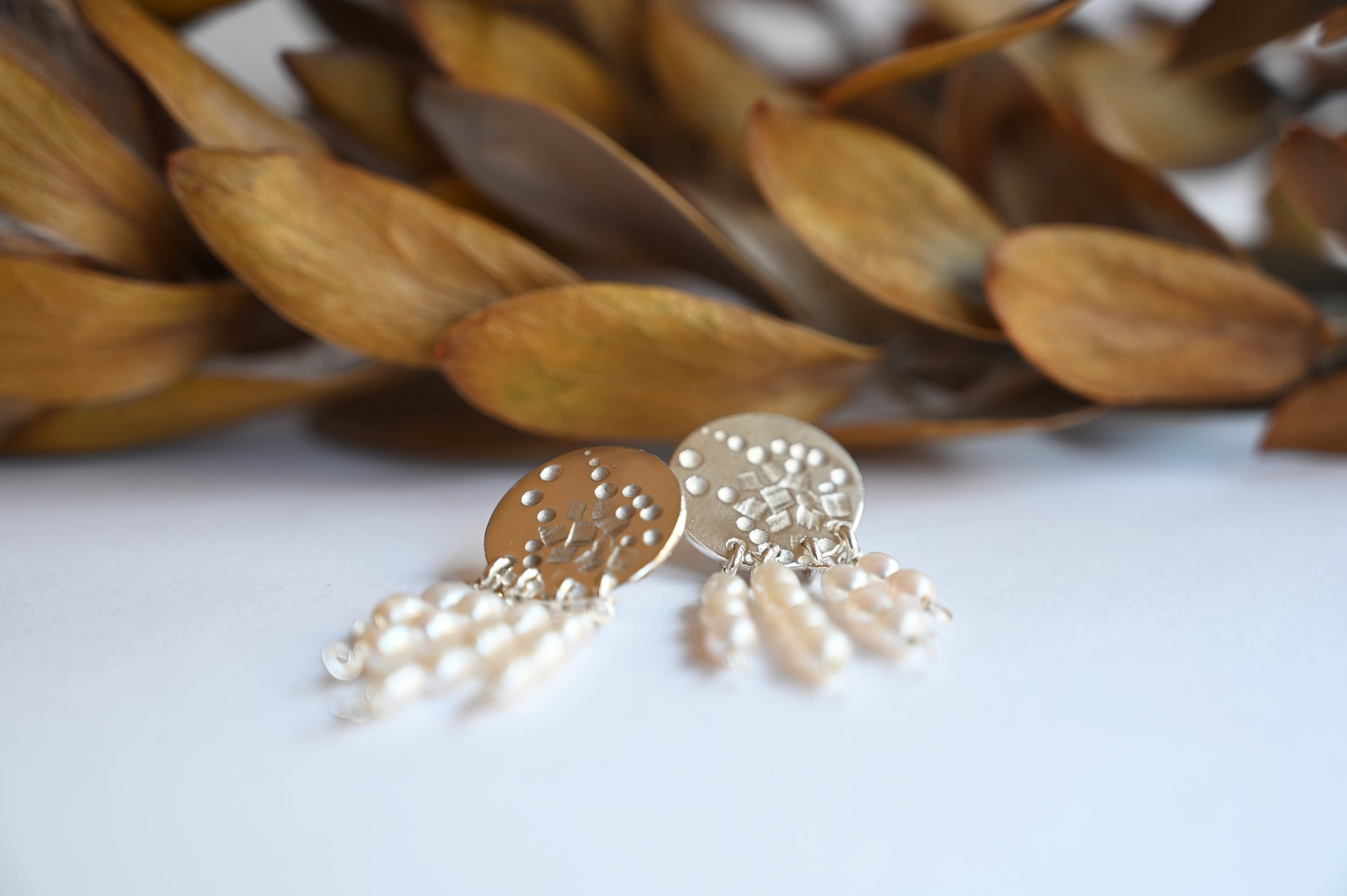 flat lay of pearl dangle studs on white ground with yellow leafs blurred in the background