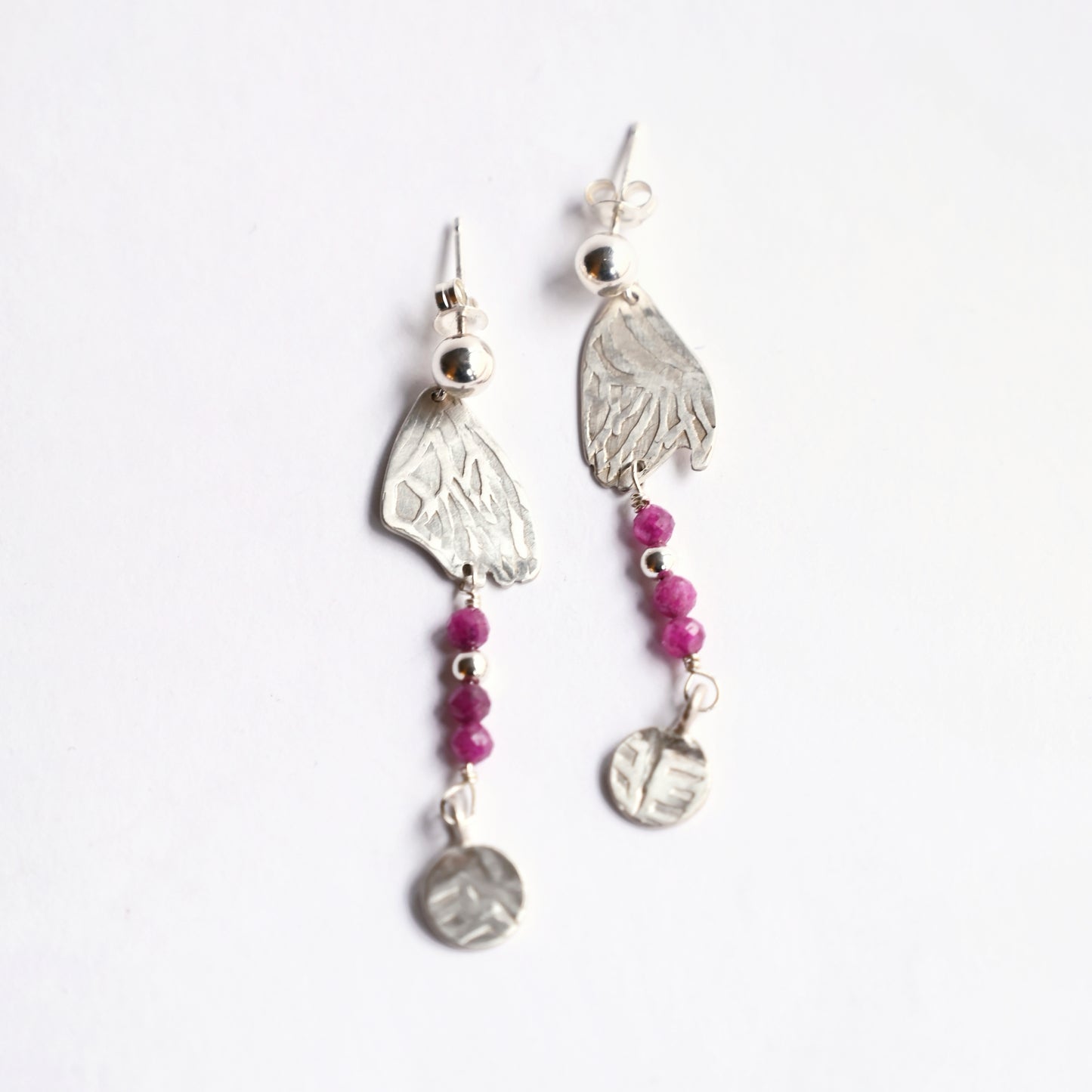 Silver dangling earrings with ruby from top on white background