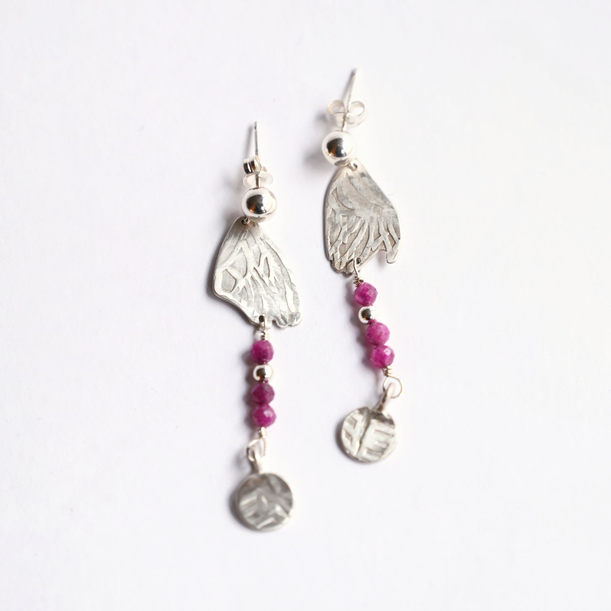 Silver dangling earrings with ruby from top on white background