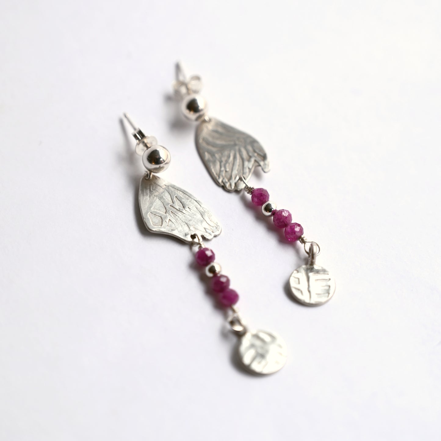 Silver dangling earrings with ruby side top view on white background