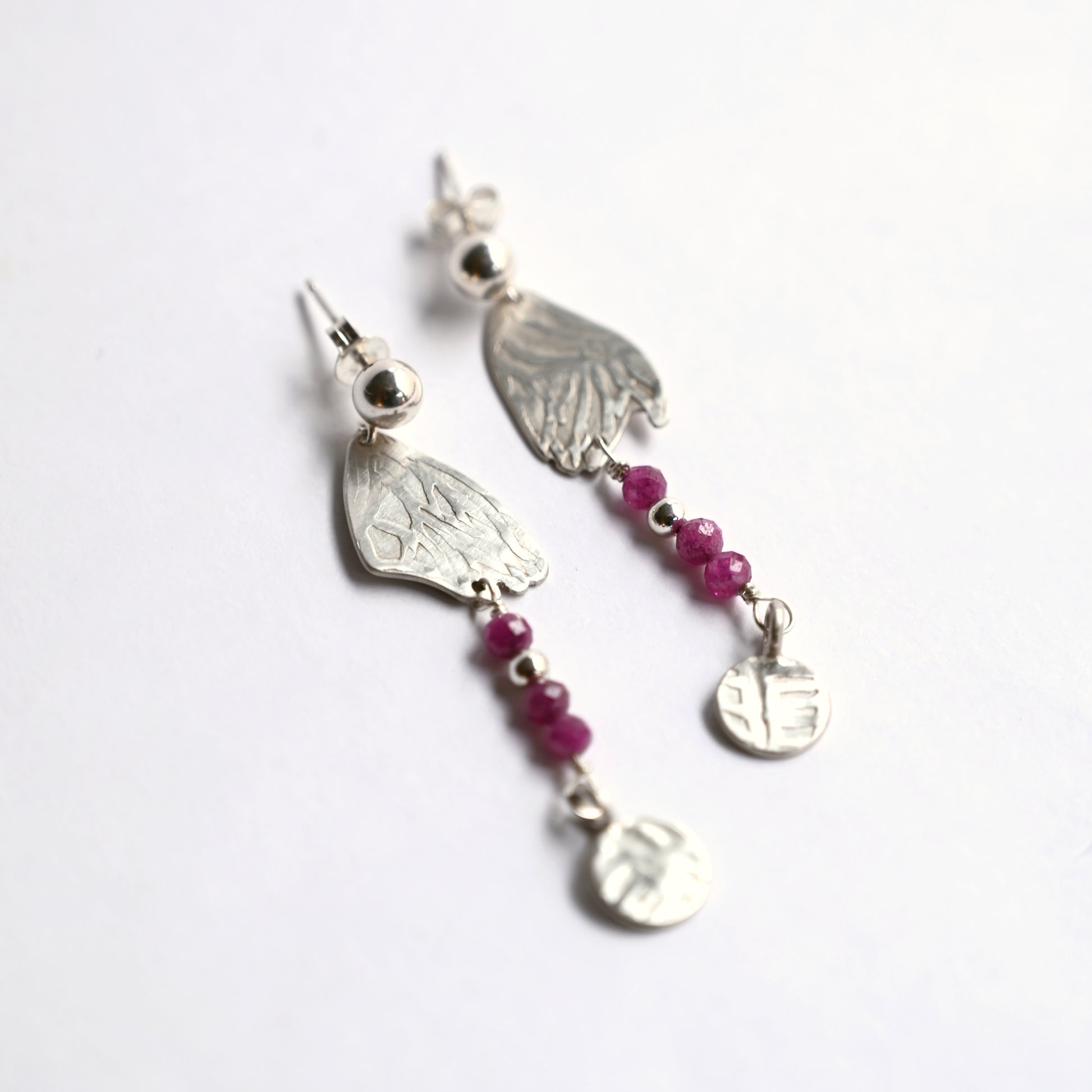 Silver dangling earrings with ruby side top view on white background