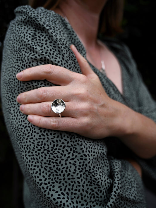 Domed disc ring in silver on model's ring finger with her hand resting on arm