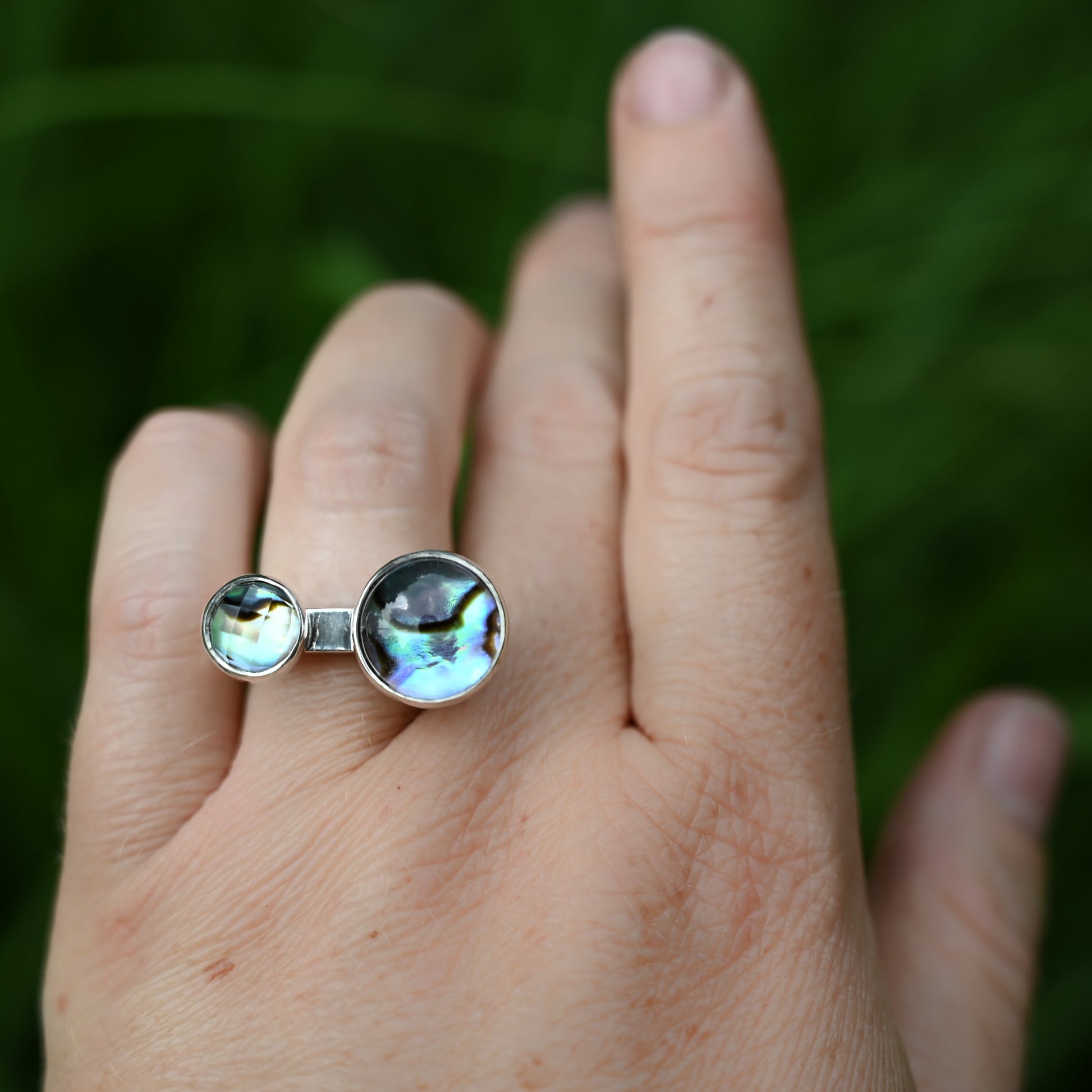 Component ring with double abalone stones on hand with top view and greenery in background