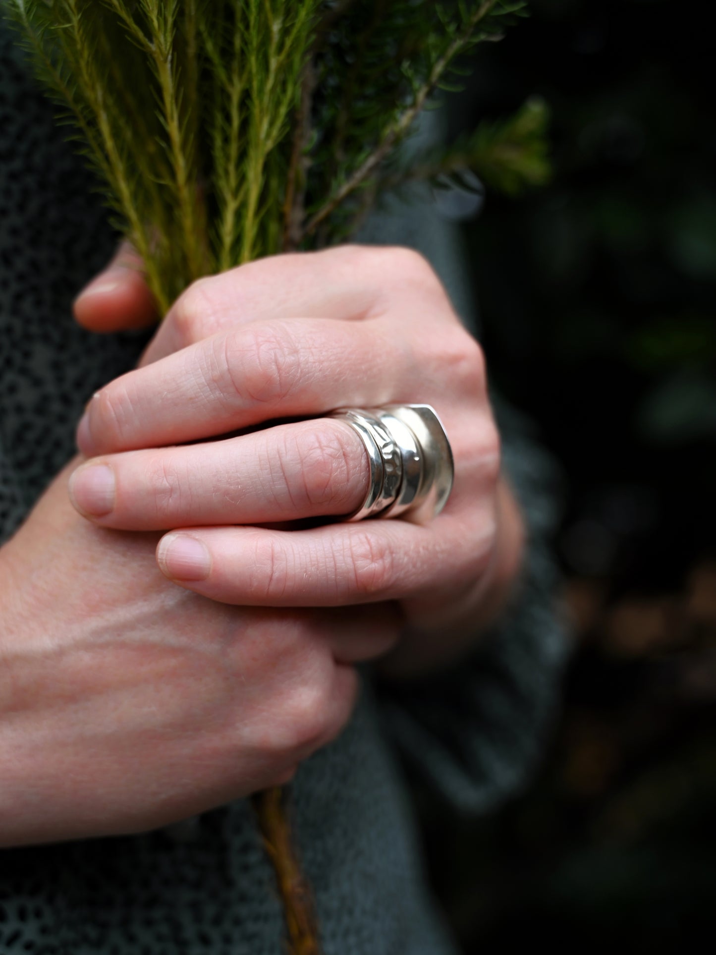 Side view of element stacking rings on hand with model holding greenery and blurred background