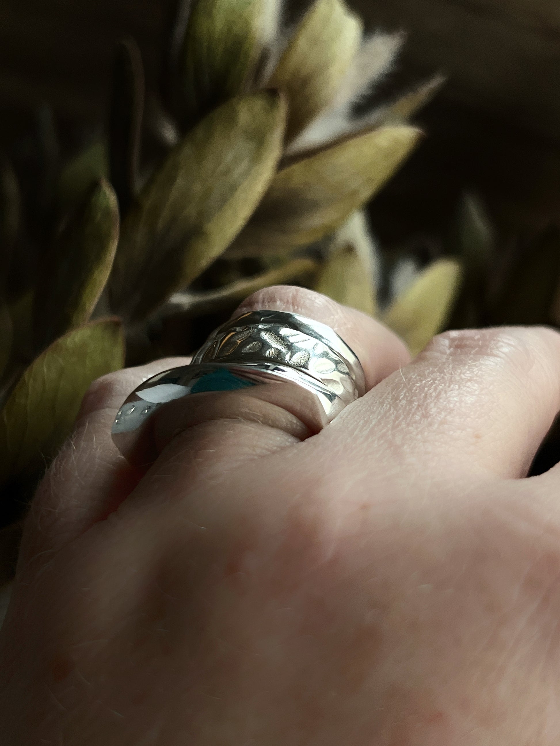 a few stacked silver rings on a ring finger with plants blurred in the background, shot with a side angle