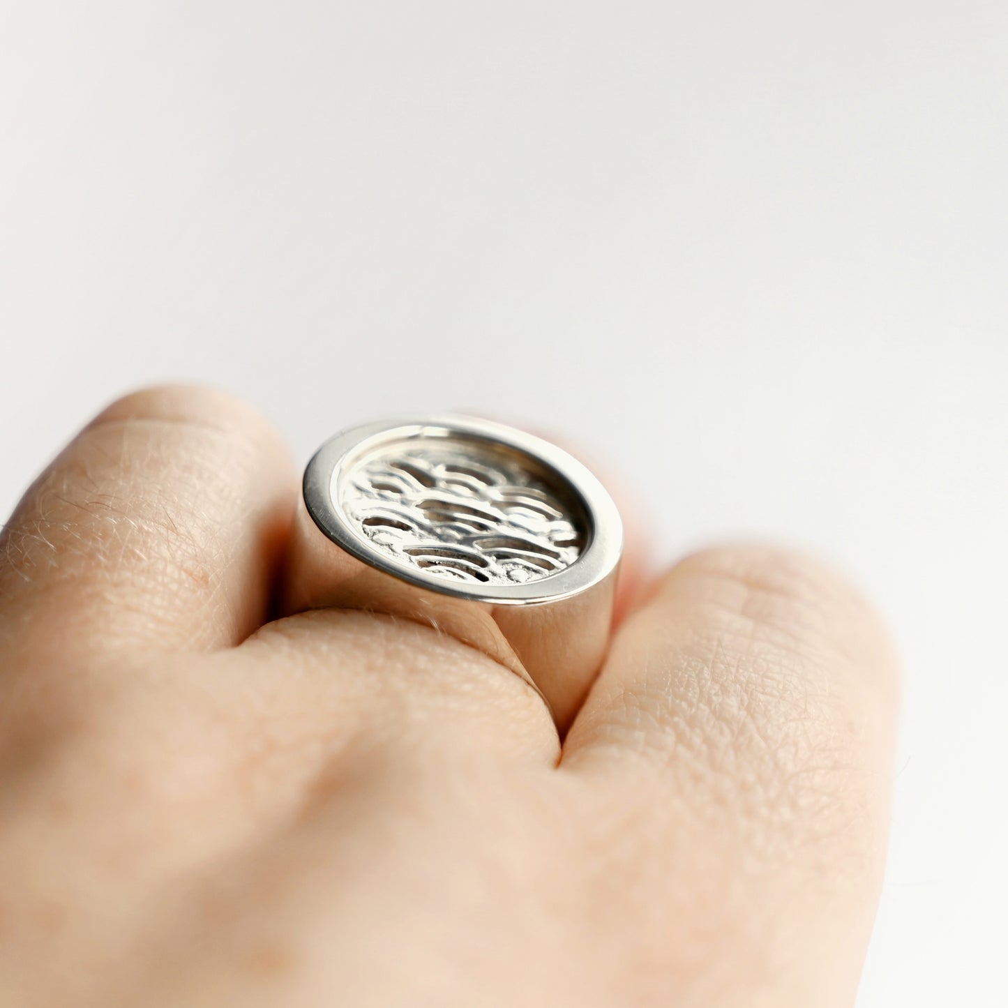 Silver node ring with cutout wave insert from side top on hand with white background