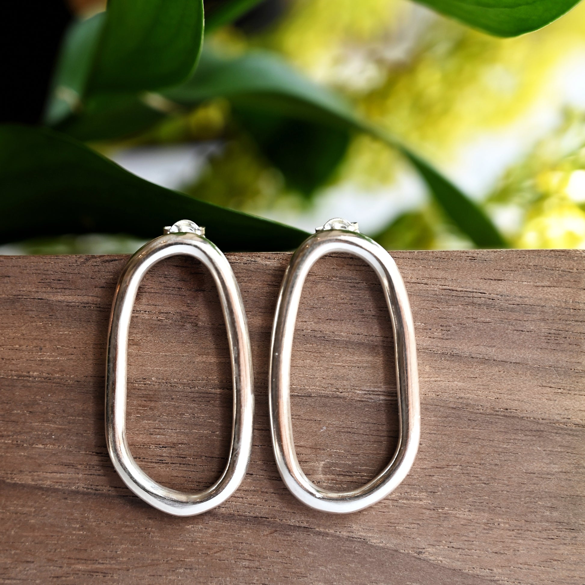 Large silver oval drop studs from front on wood block