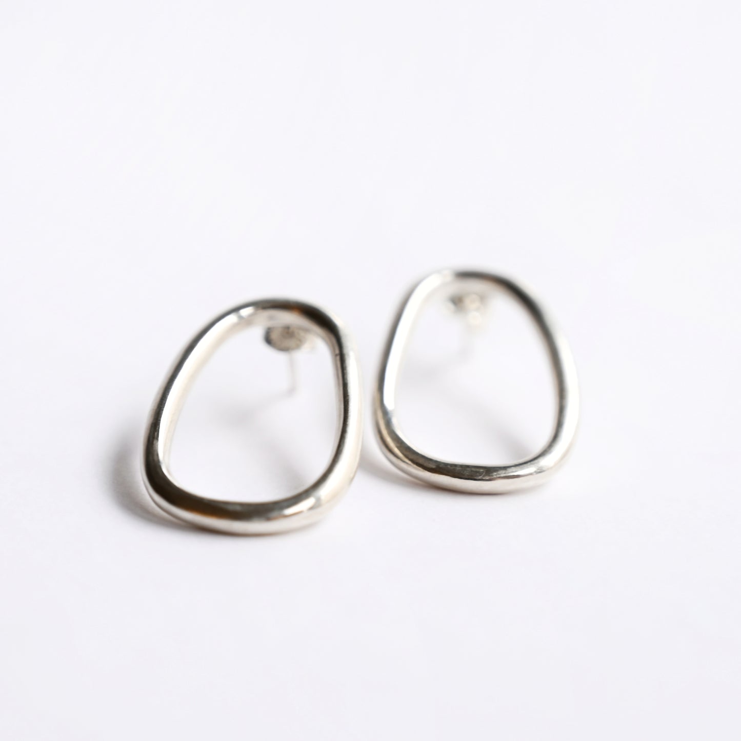Small silver oval drop studs from front and side on white background