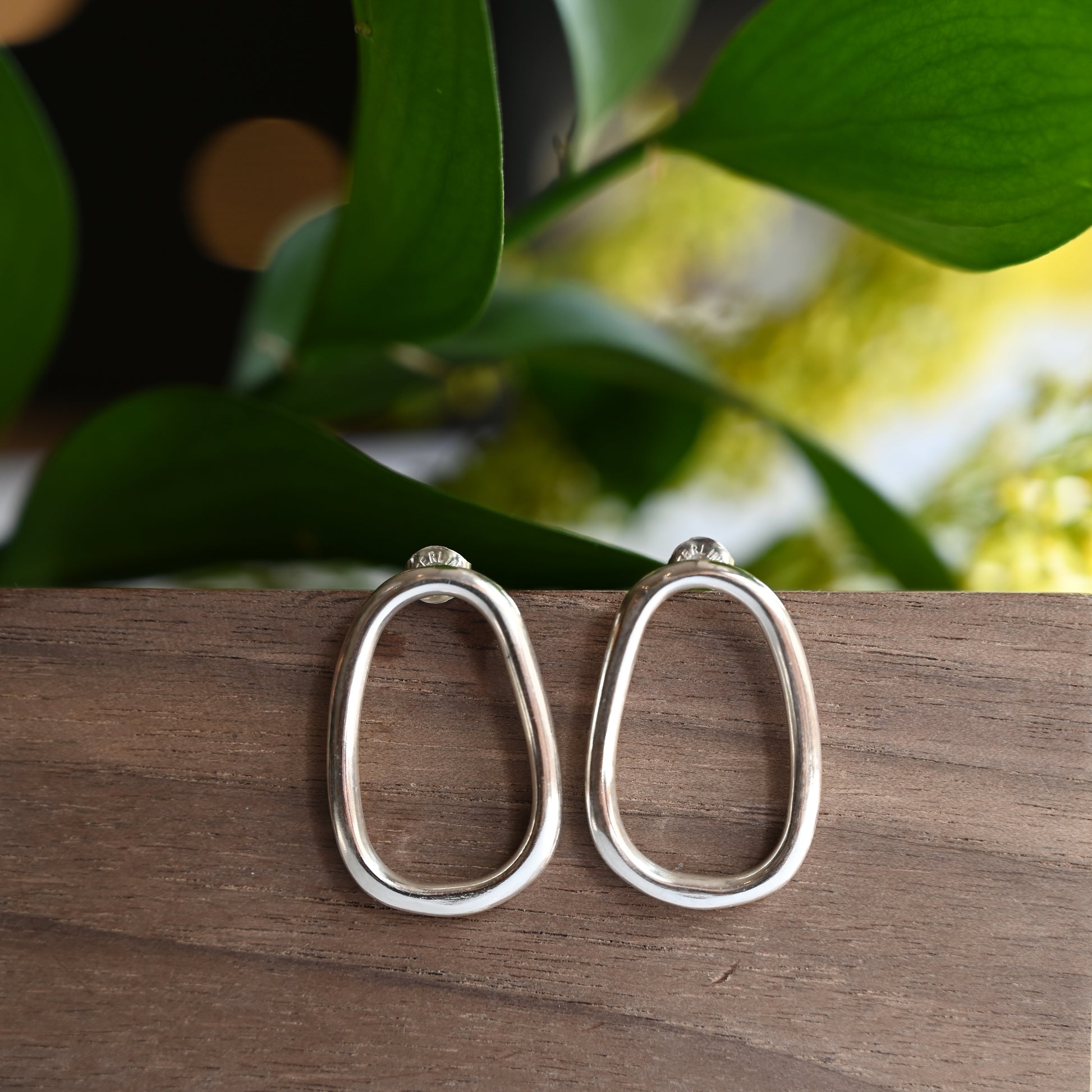 Small silver oval drop studs on wooden block with greenery in background
