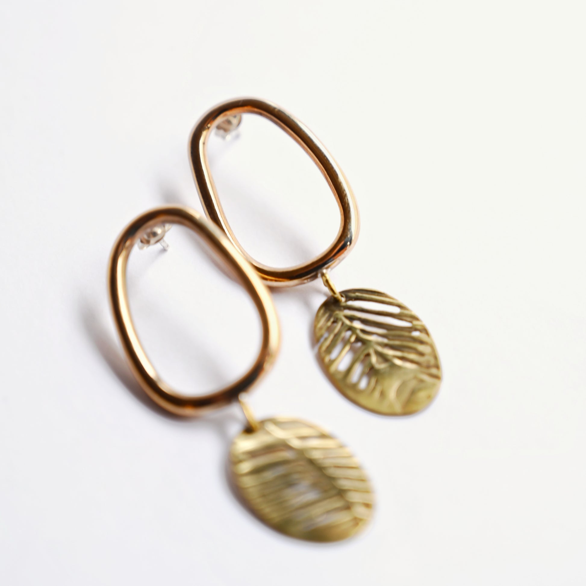 Bronze oval drop earrings with cutout leaf discs from front on white background