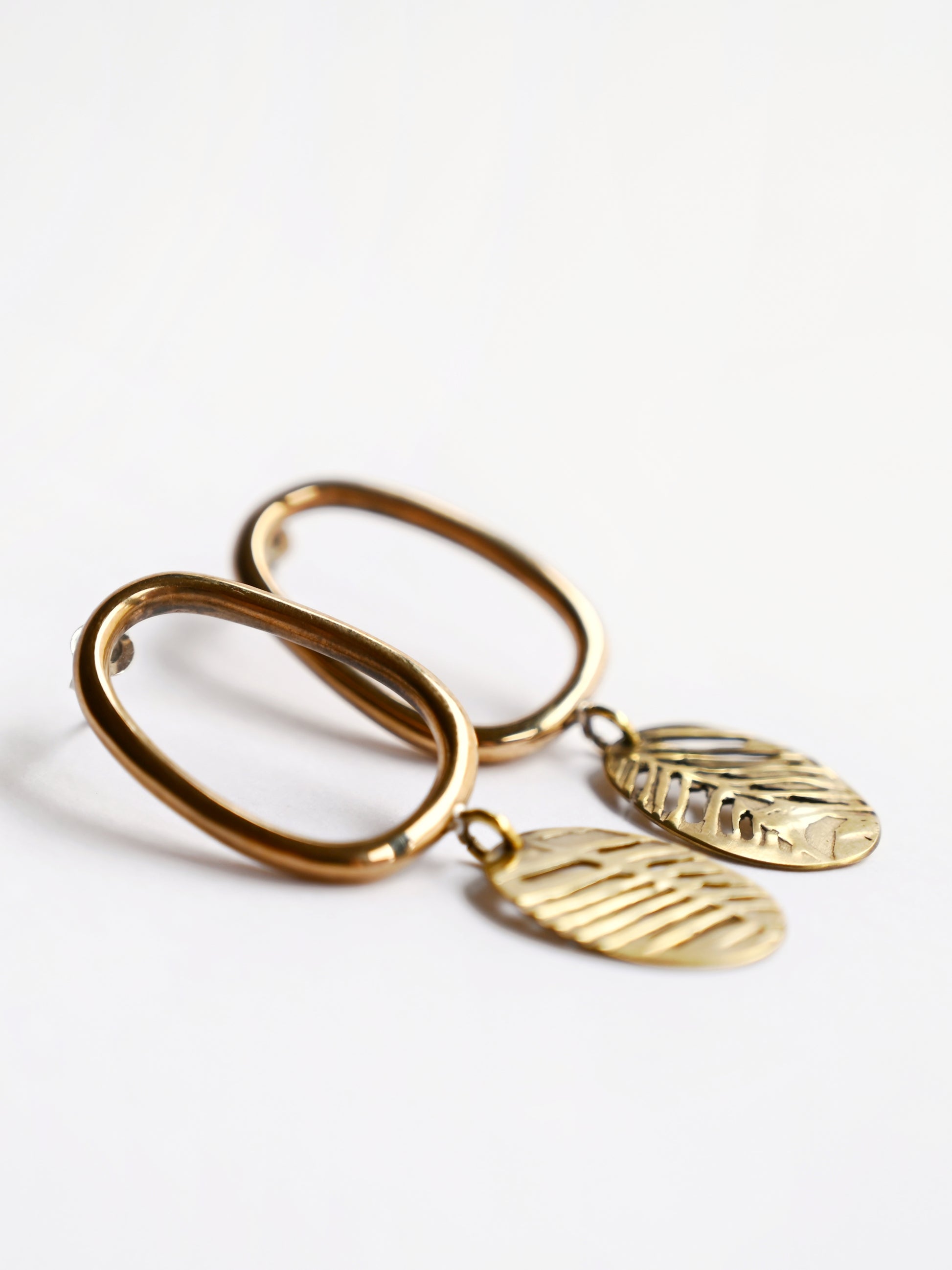Bronze oval drop earrings with cutout leaf disc from side on white background