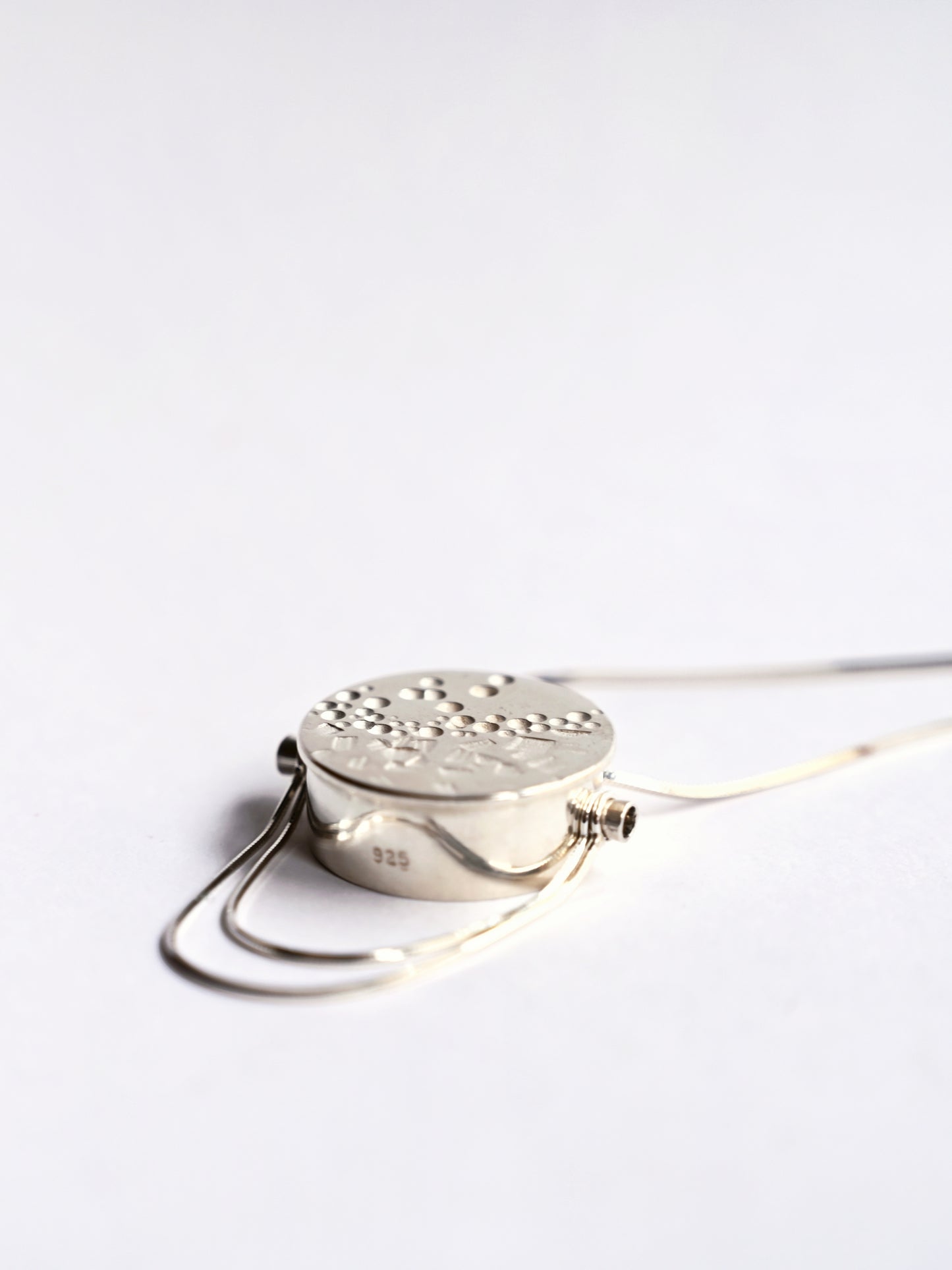 Side view of small silver contrast box pendant with snake chains on tube on white background