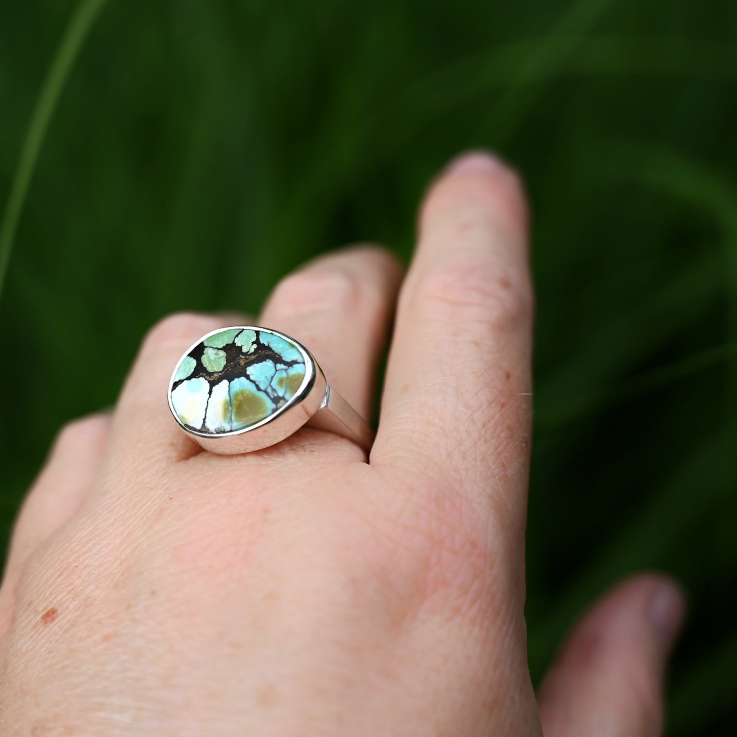Sterling silver component ring with Cloud mountain turquoise on middle finger with greenery in background.
